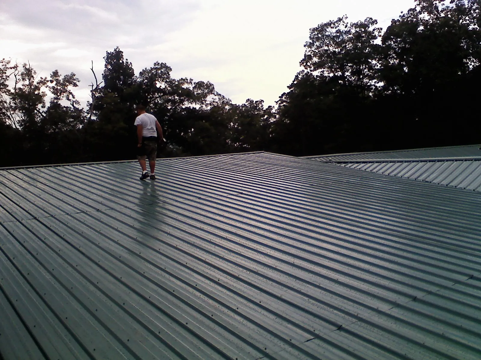 Roofer walking a wide expanse of new green metal roofing in Chatham